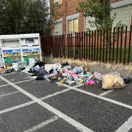 Discarica davanti alla scuola: rifiuti vicino al container per gli abiti usati