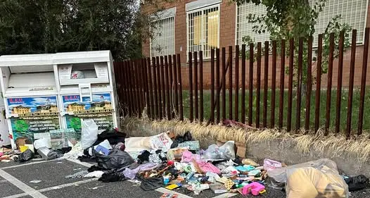 Discarica davanti alla scuola: rifiuti vicino al container per gli abiti usati