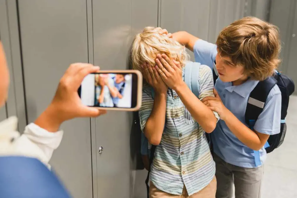 Schoolchildren cruel boys filming on the phone torturing bullying their classmate in school hall. Puberty difficult age , InsideCreativeHouse - stock.adob